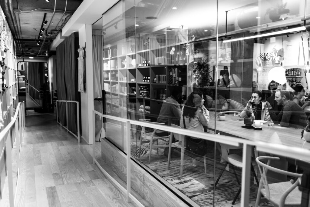 Black and white photo of people enjoying drinks at a conference table behind a glass wall, set beside a wooden ramp.
